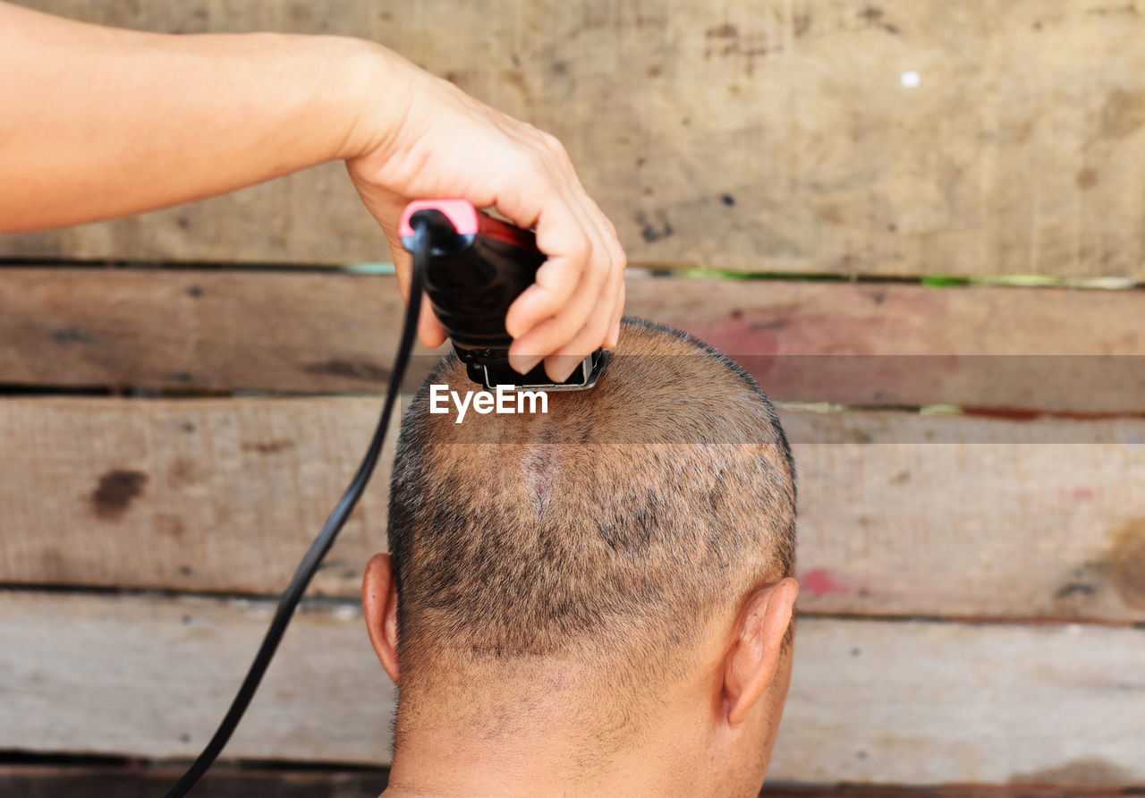 Cropped image of barber shaving head of man outdoors