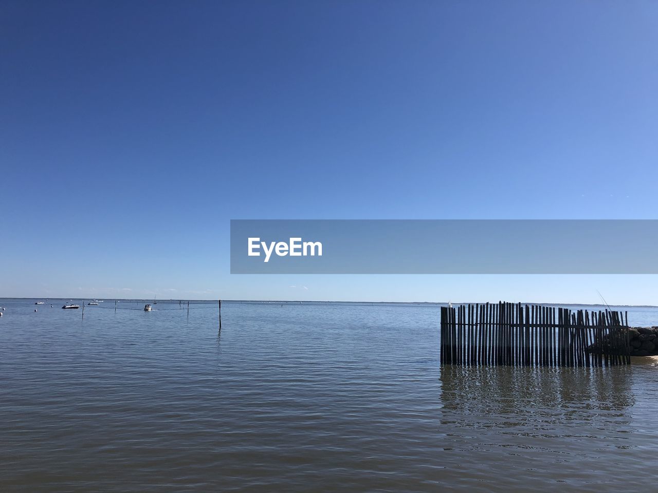 WOODEN POSTS IN SEA AGAINST CLEAR SKY