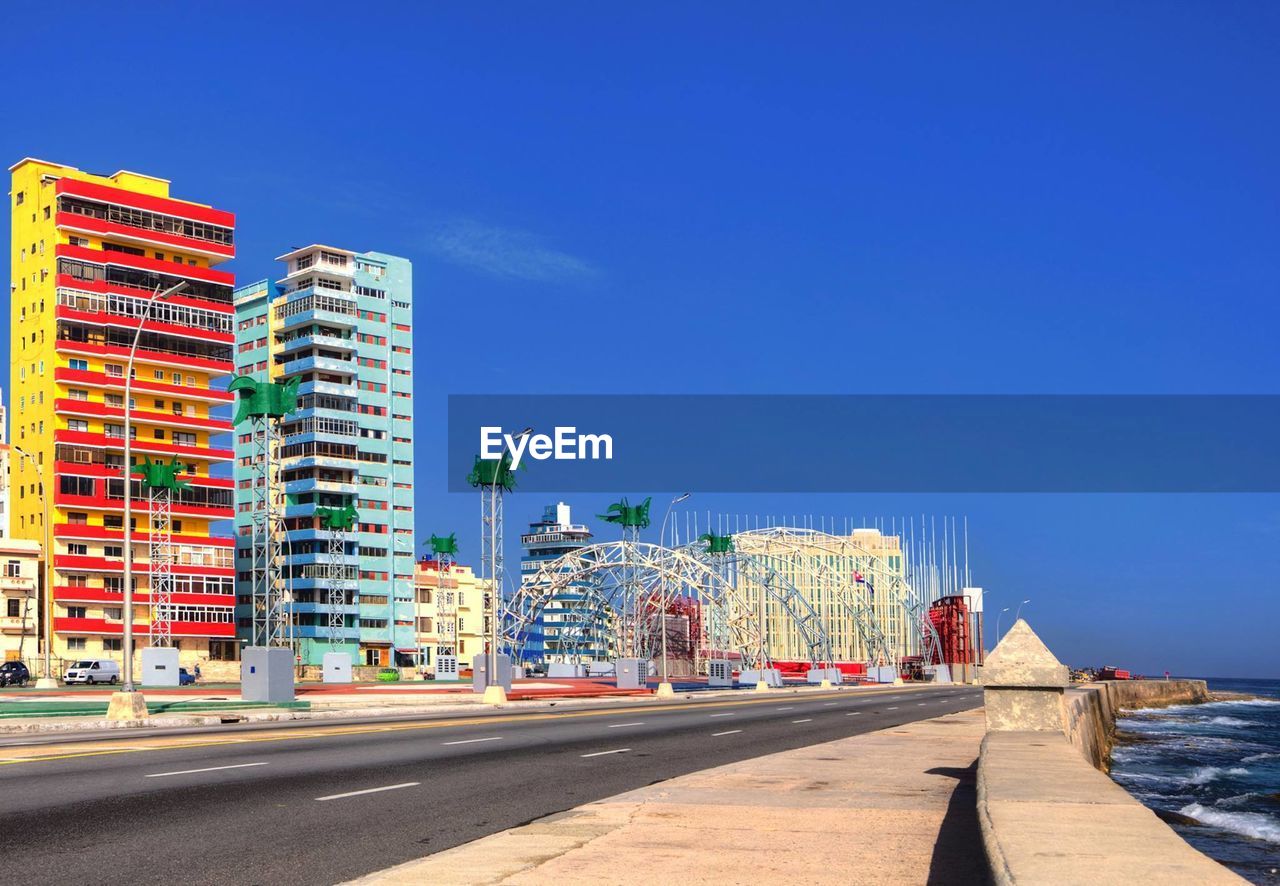 Road by buildings against blue sky