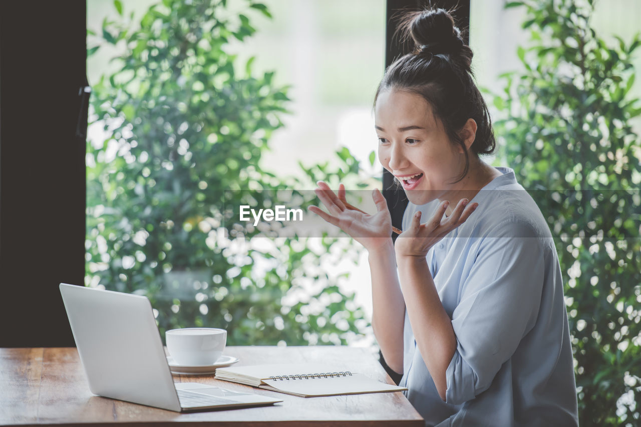 WOMAN USING MOBILE PHONE WHILE SITTING AT TABLE