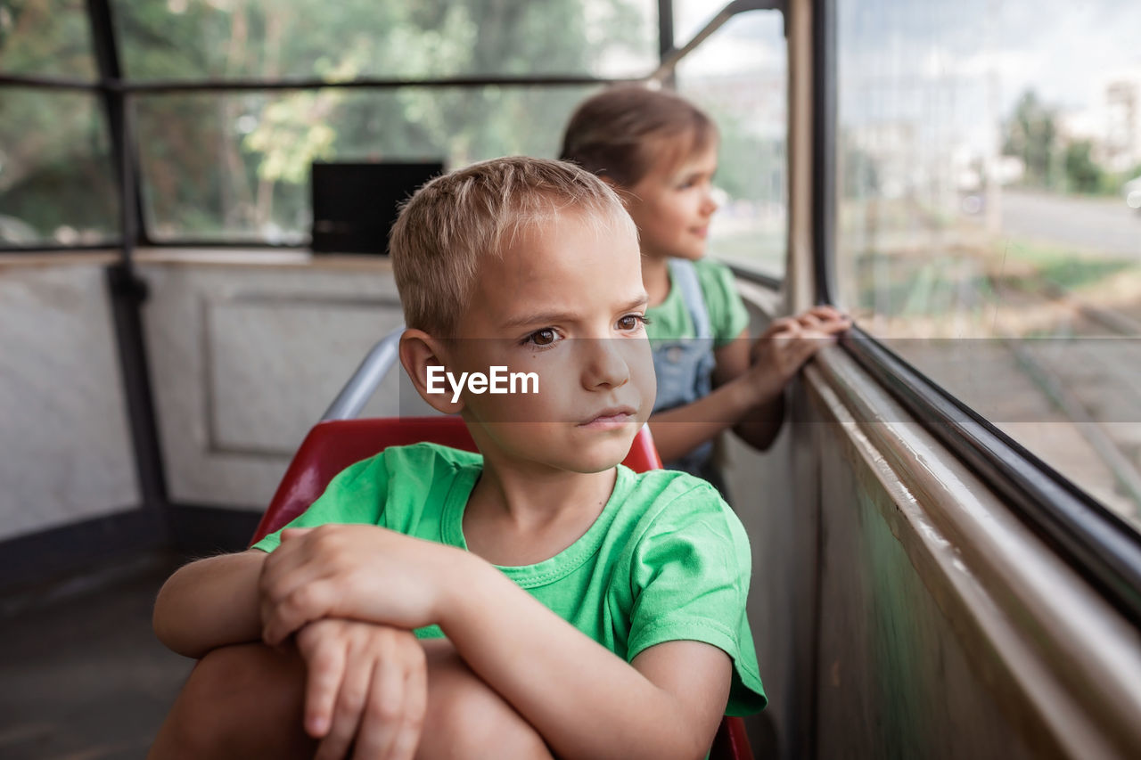 Kids ride in empty tram and look at the window attentively, public transportation, city tramway