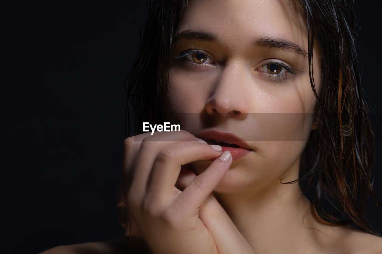 Close-up portrait of beautiful young woman over black background