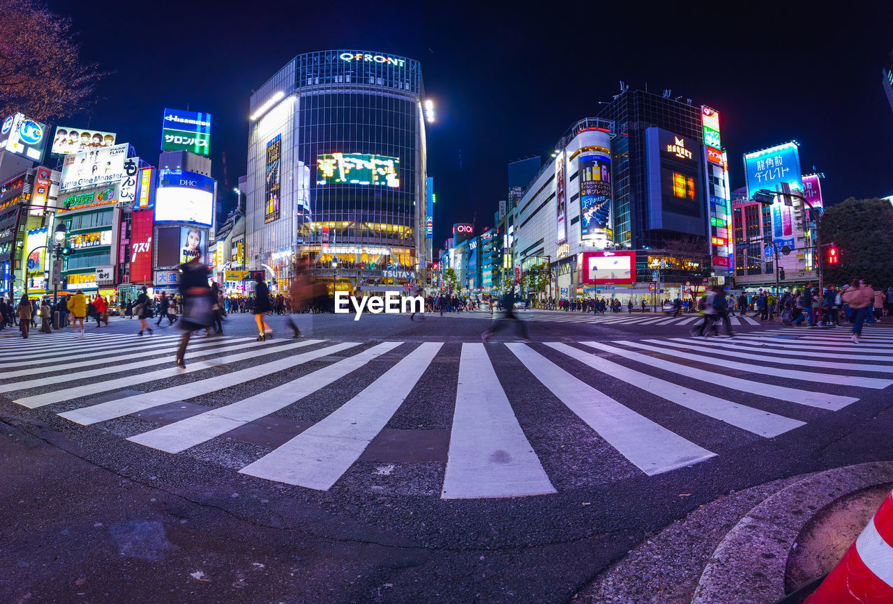 People crossing road in city at night at shibuya crossing , tokyo , japan