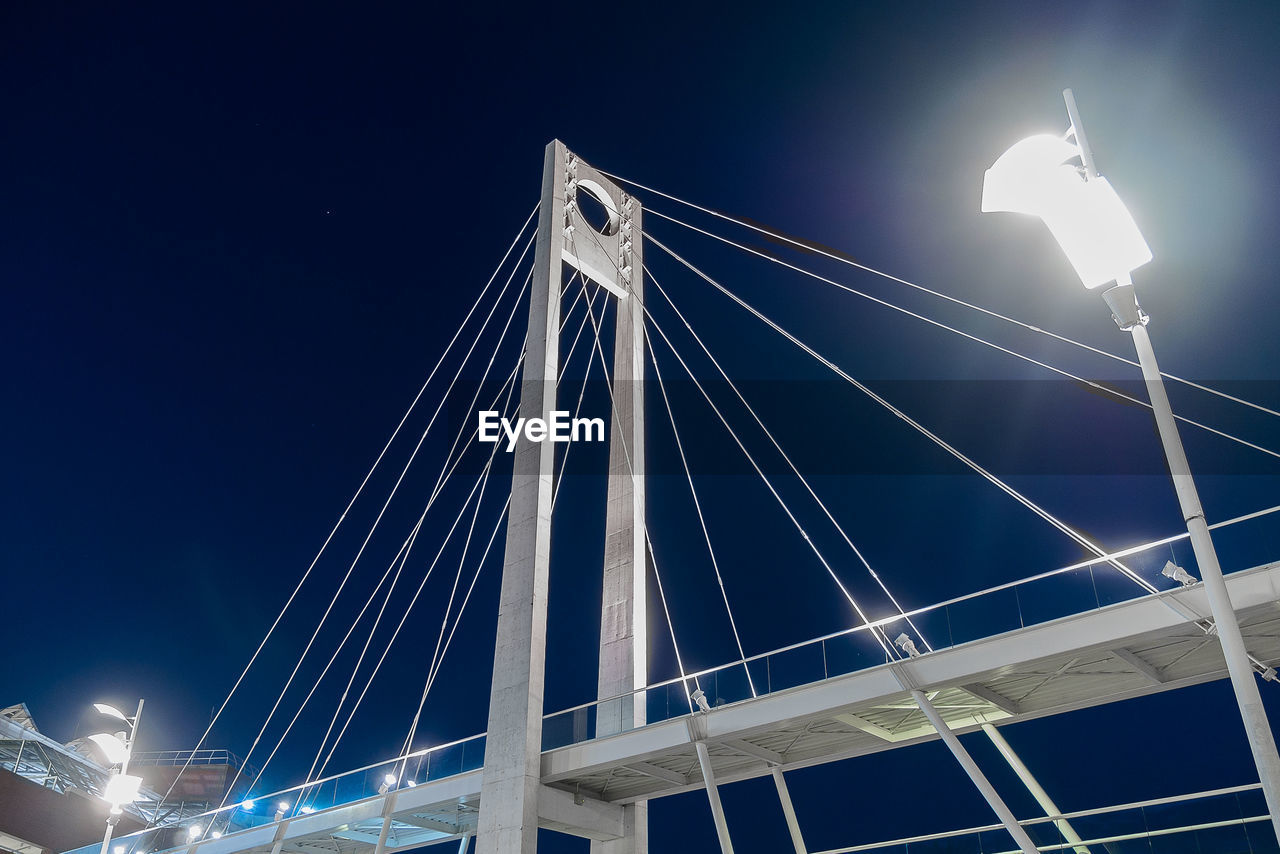 LOW ANGLE VIEW OF ILLUMINATED BRIDGE AT NIGHT