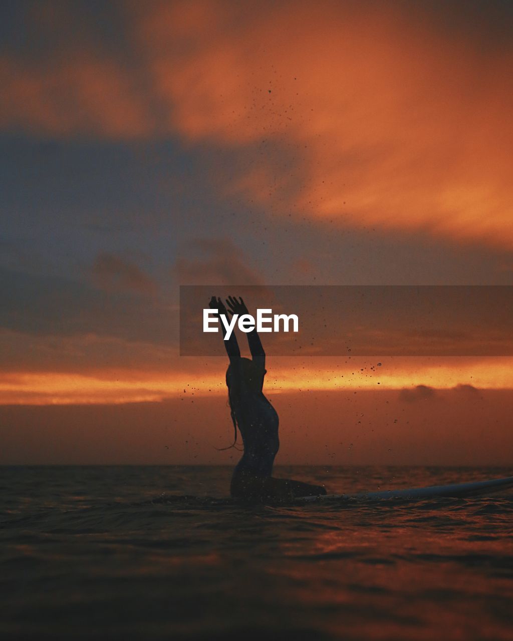 Silhouette young woman surfing on sea against cloudy sky during sunset