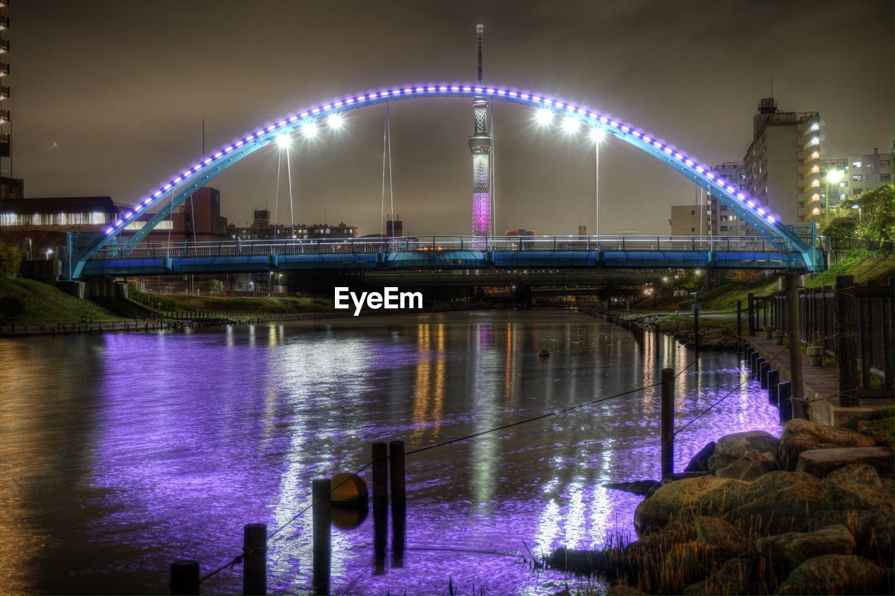 Illuminated bridge over river against sky in city at night