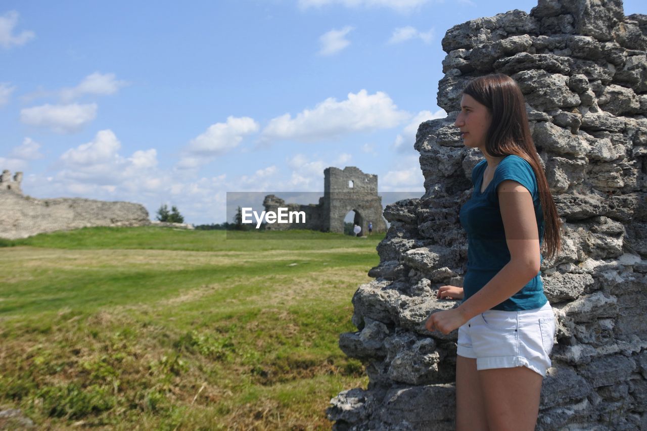 Side view of woman standing on field against ancient castle