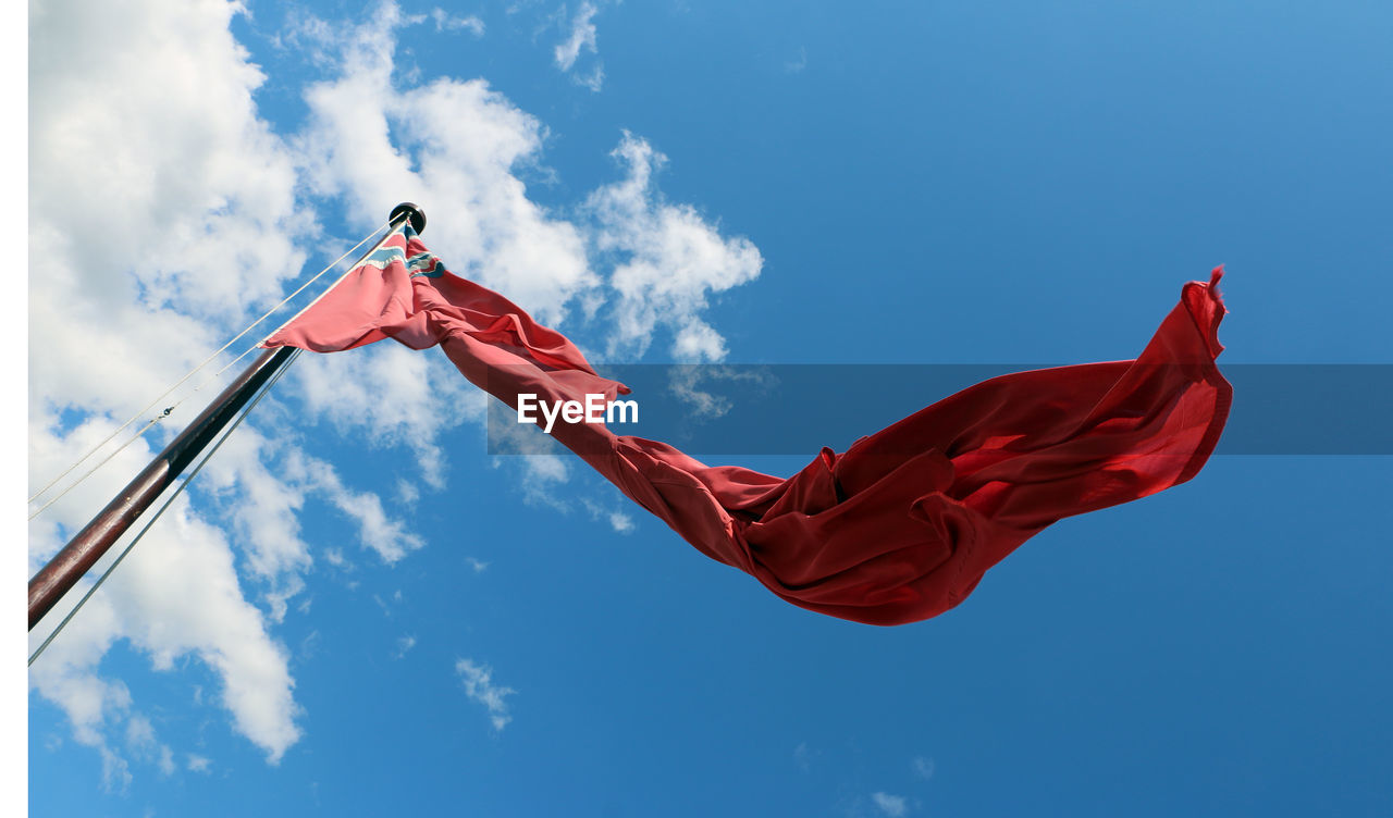 Low angle view of torn flag against blue sky