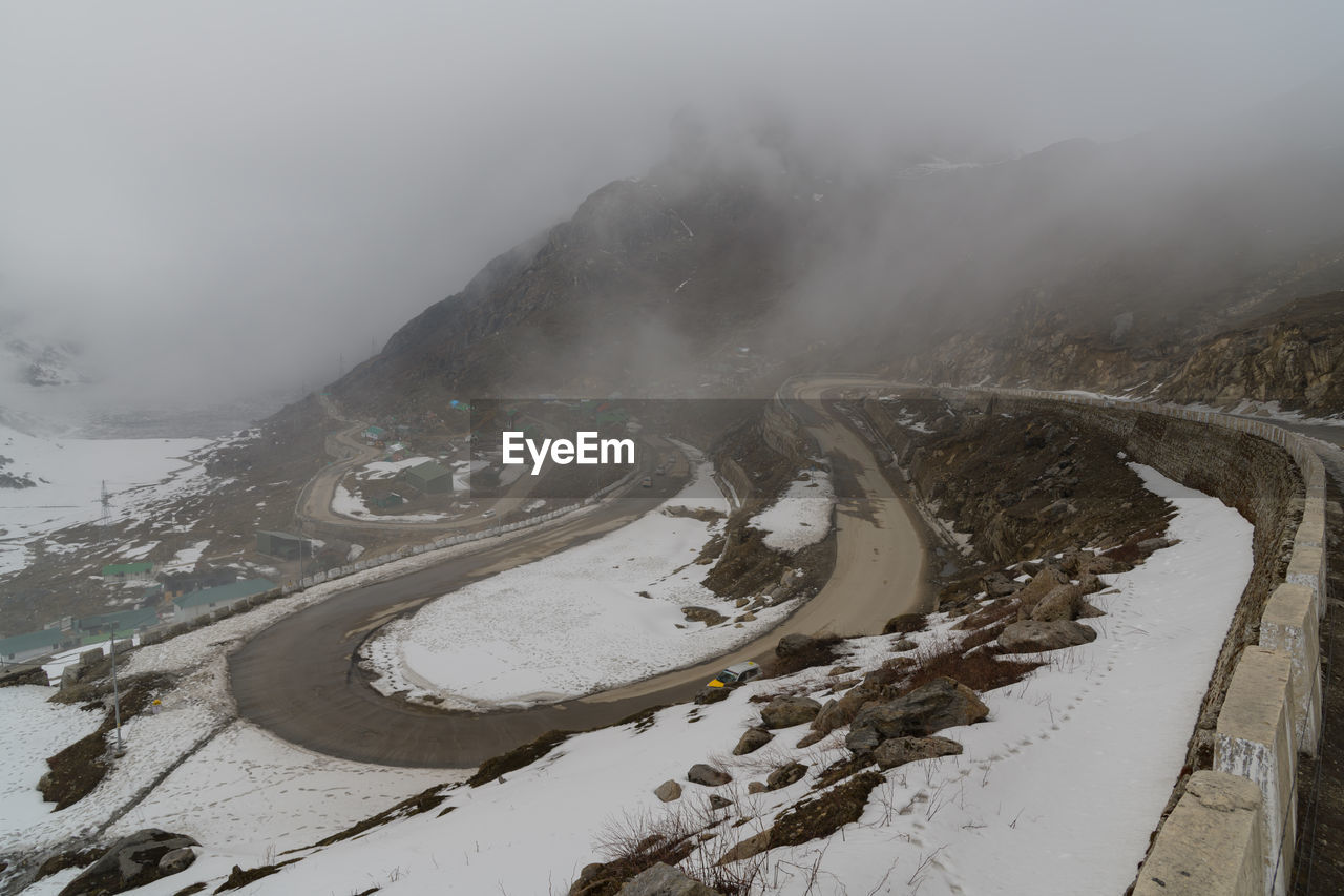 environment, snow, cold temperature, winter, fog, mountain, landscape, scenics - nature, nature, travel, beauty in nature, road, land, transportation, travel destinations, mountain range, sky, no people, cloud, water, tourism, outdoors, winding road, social issues, tranquility, overcast, architecture, mountain pass, non-urban scene, atmospheric mood, curve, ice, frozen, snowcapped mountain, valley, mountain peak, day, mountain road