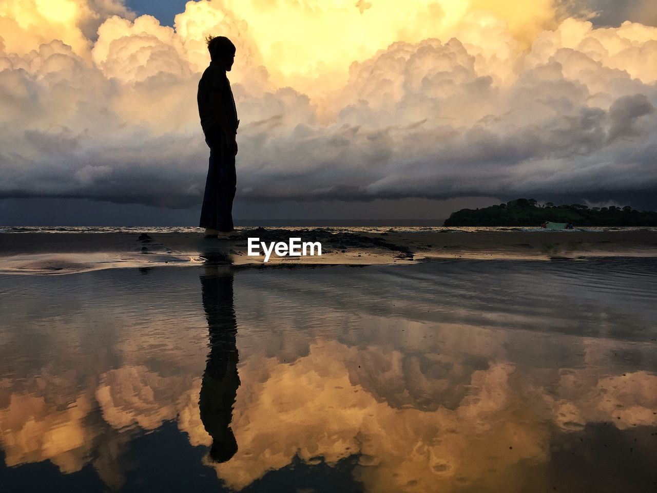 Silhouette man standing on shore against cloudy sky during sunset