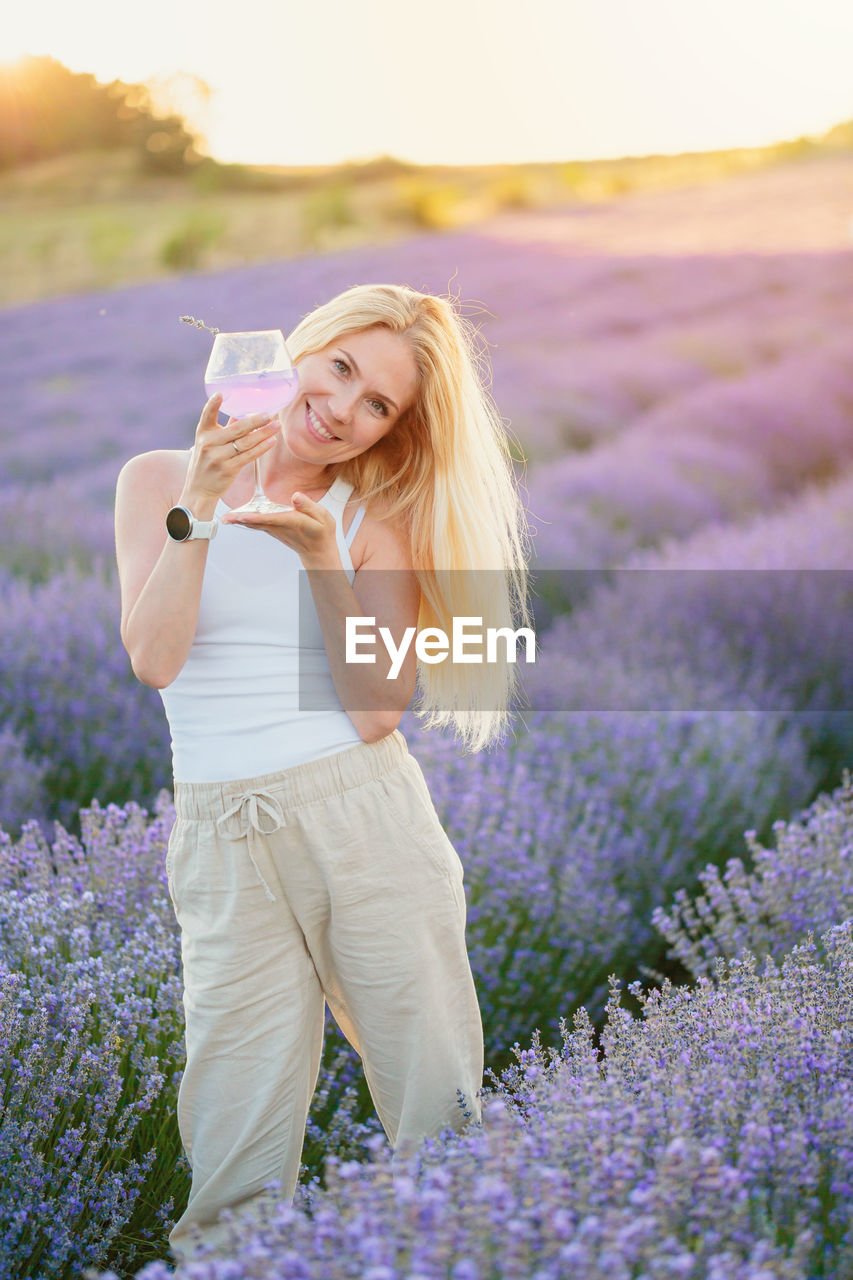 portrait of young woman drinking water while standing on field