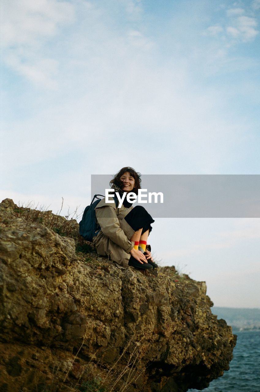 Low angle view of woman sitting on rock against sky
