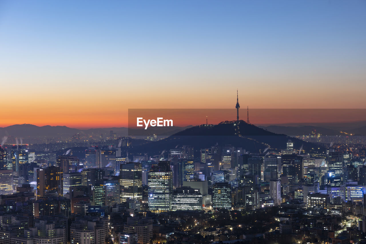 Illuminated buildings in city against sky during sunset