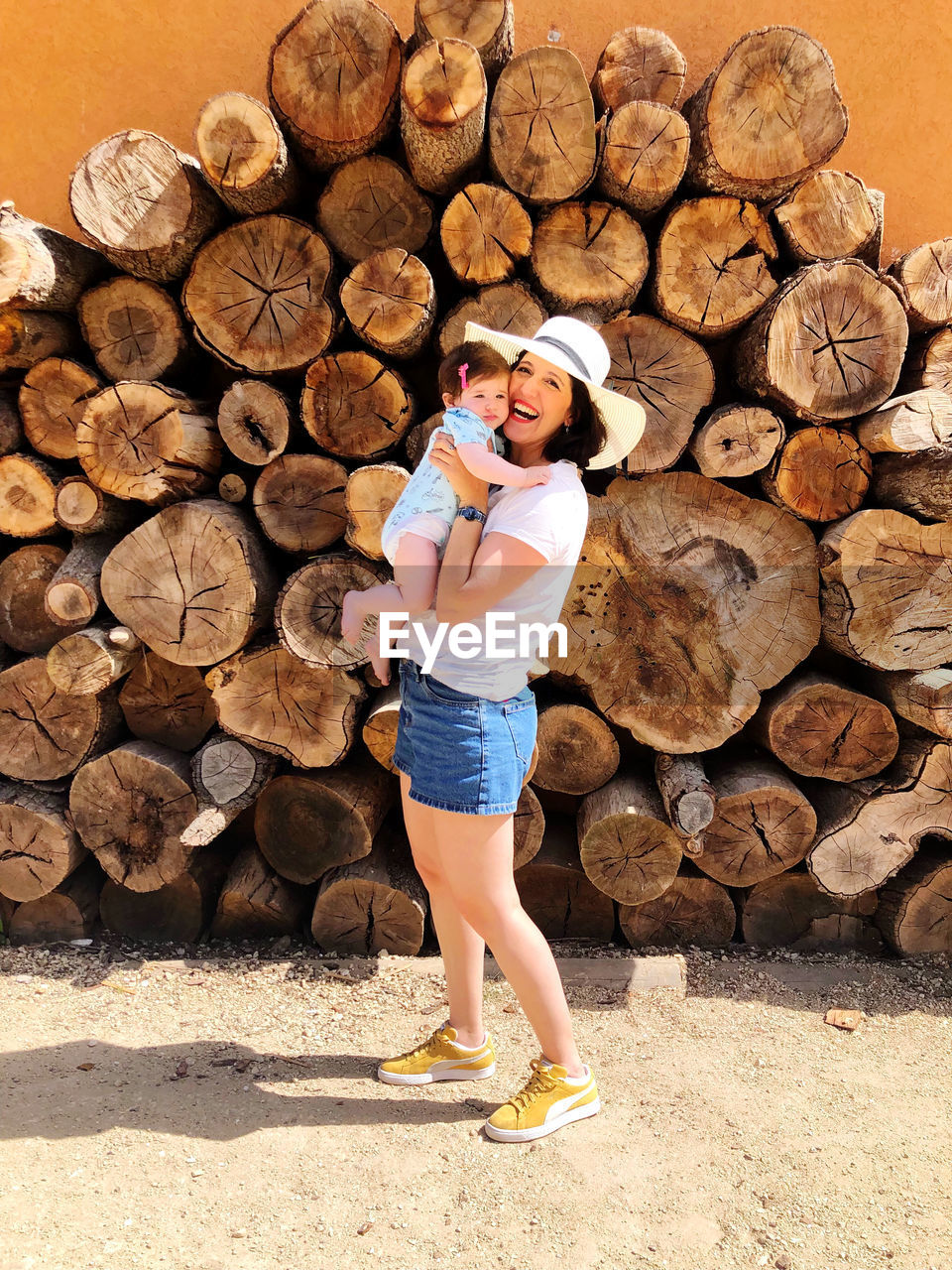 Full length of woman standing on wooden logs holding her baby