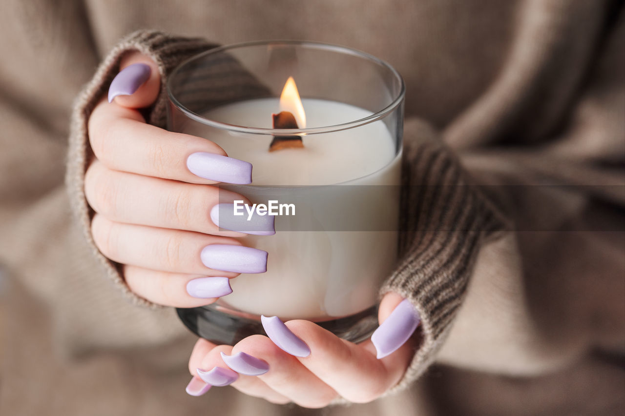 The hands of a young girl with a beautiful light purple manicure hold a candle. 