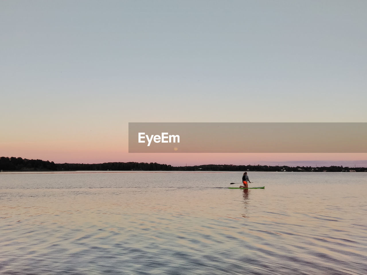 Woman paddleboarding in sea against clear sky during sunset