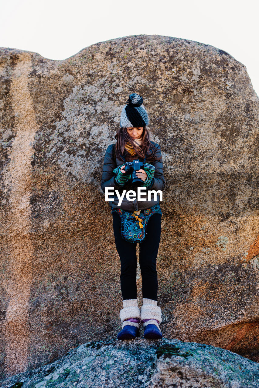 Full length of woman holding camera standing against wall