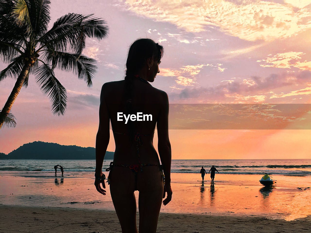 Rear view of woman standing at beach against sky during sunset