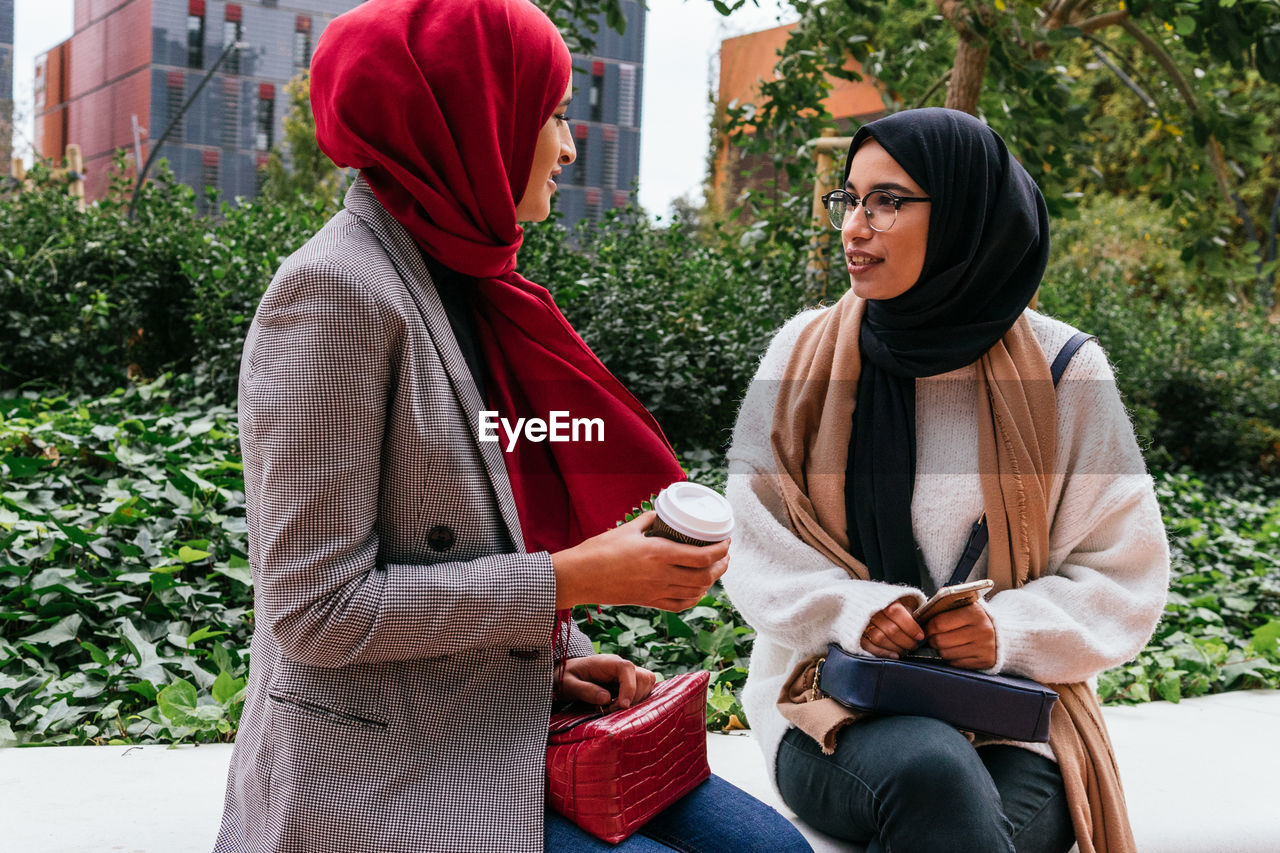 Friendly arab female friends sitting on street and talking to each other while enjoying weekend together