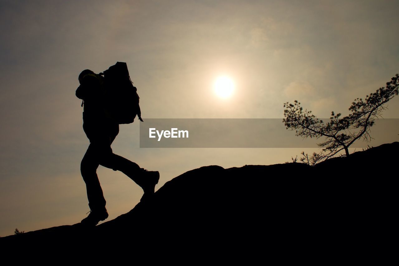 Tourist with sporty backpack and poles in hands stand on cliff and watching into deep misty valley 