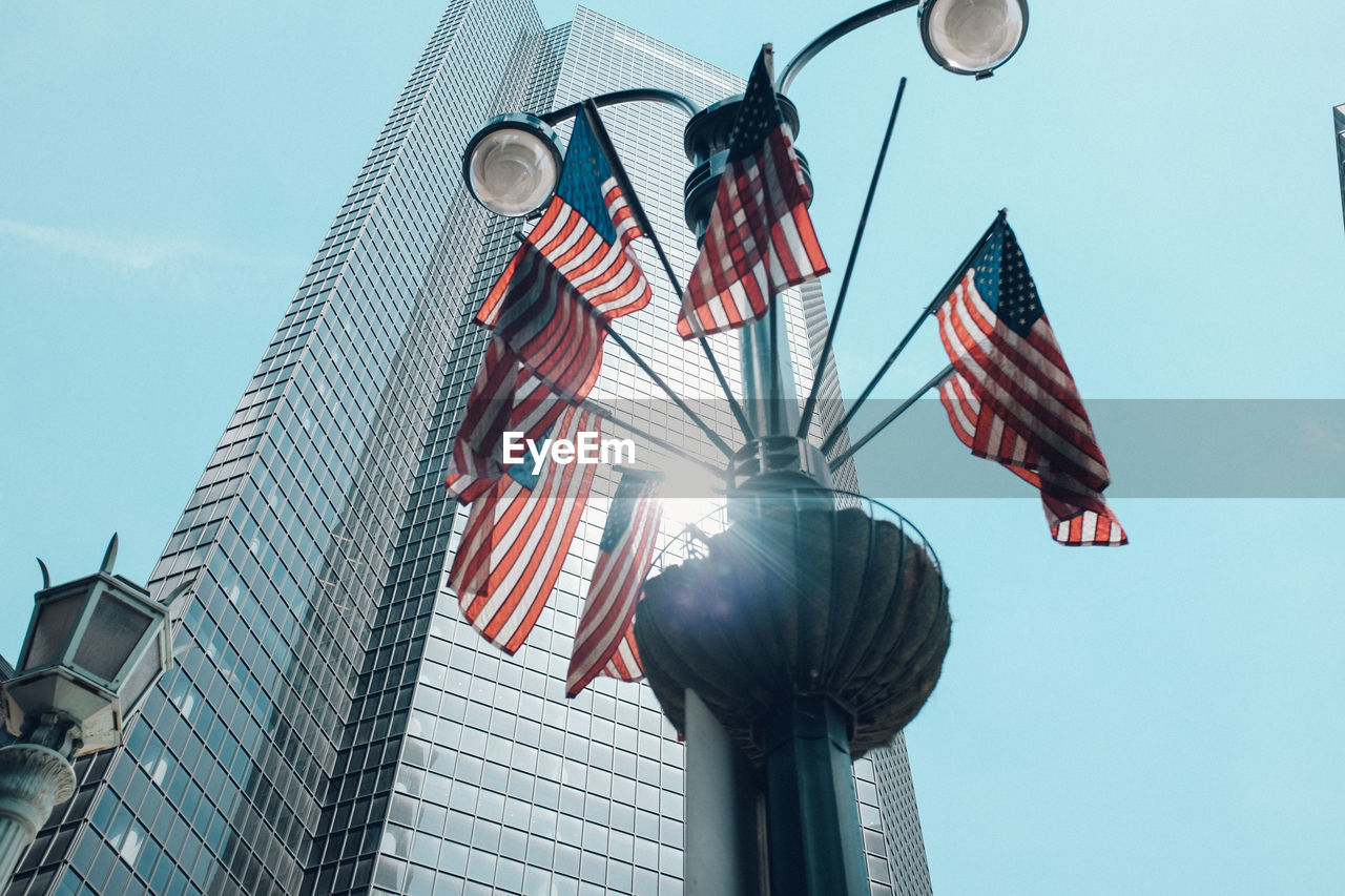 Low angle view of american flags by skyscraper against sky