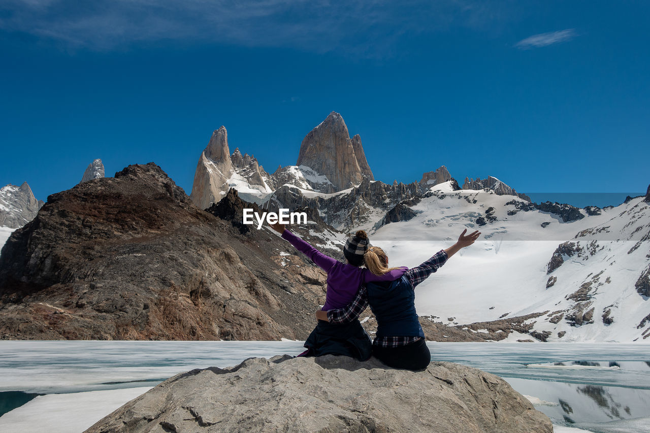 Man sitting on rock by mountain against sky