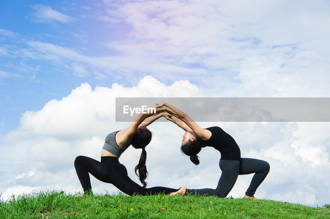 Women exercising on grassy field against cloudy sky at park