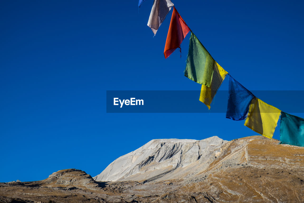 Low angle view of prayer flags hanging against clear blue sky