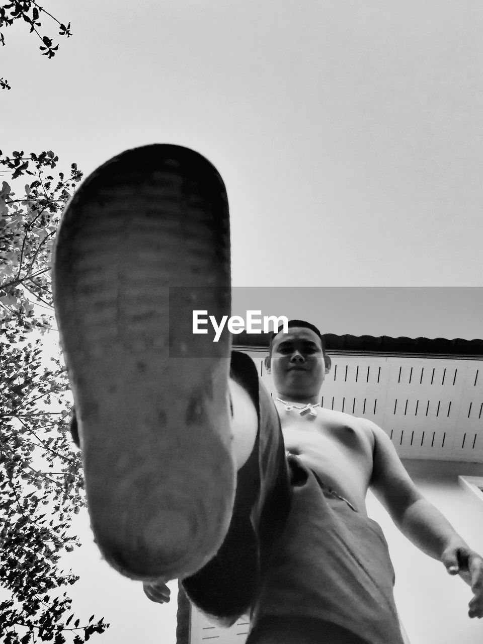 LOW ANGLE PORTRAIT OF MAN HOLDING SUNGLASSES AGAINST SKY