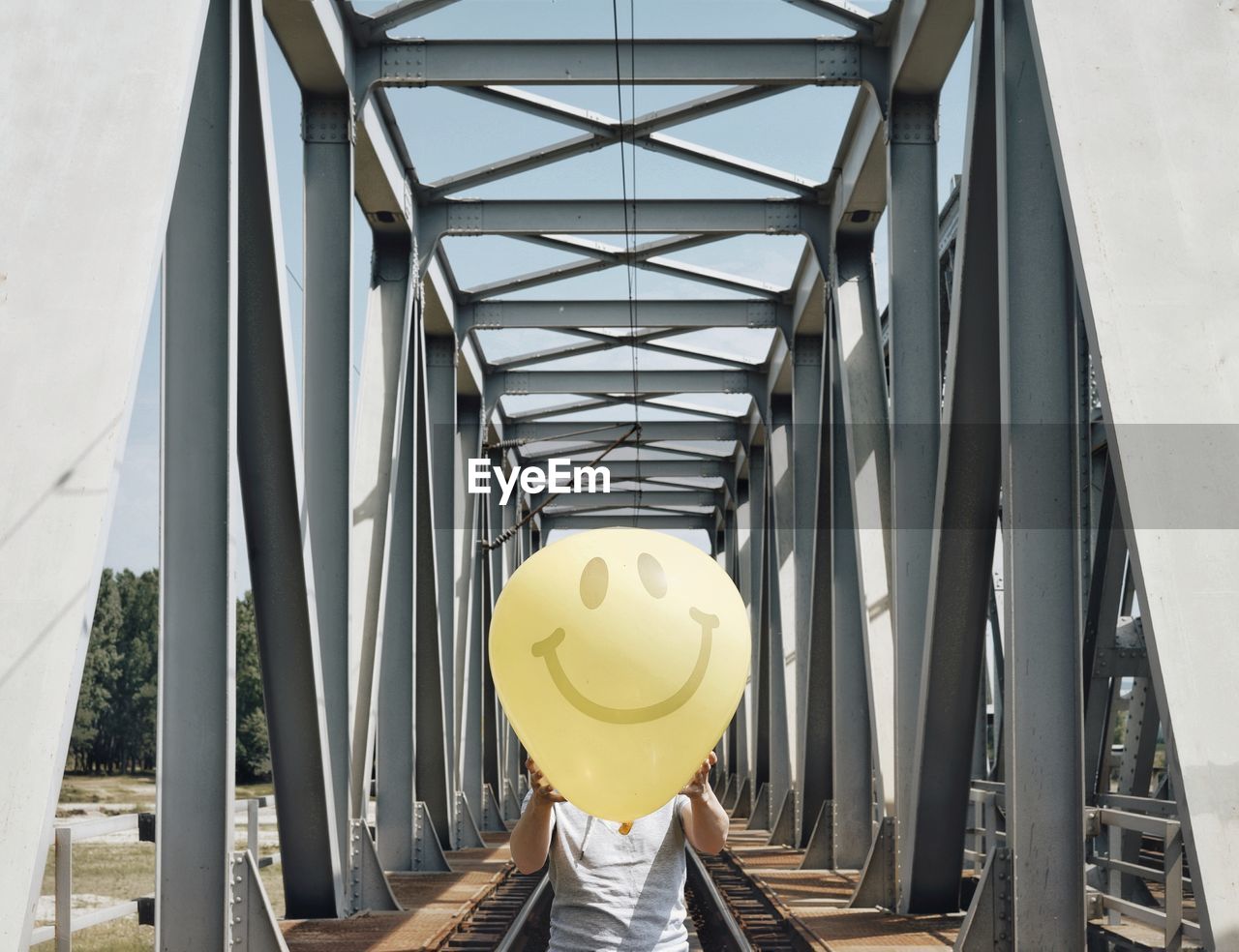 Man holding smiley face balloon on railway bridge