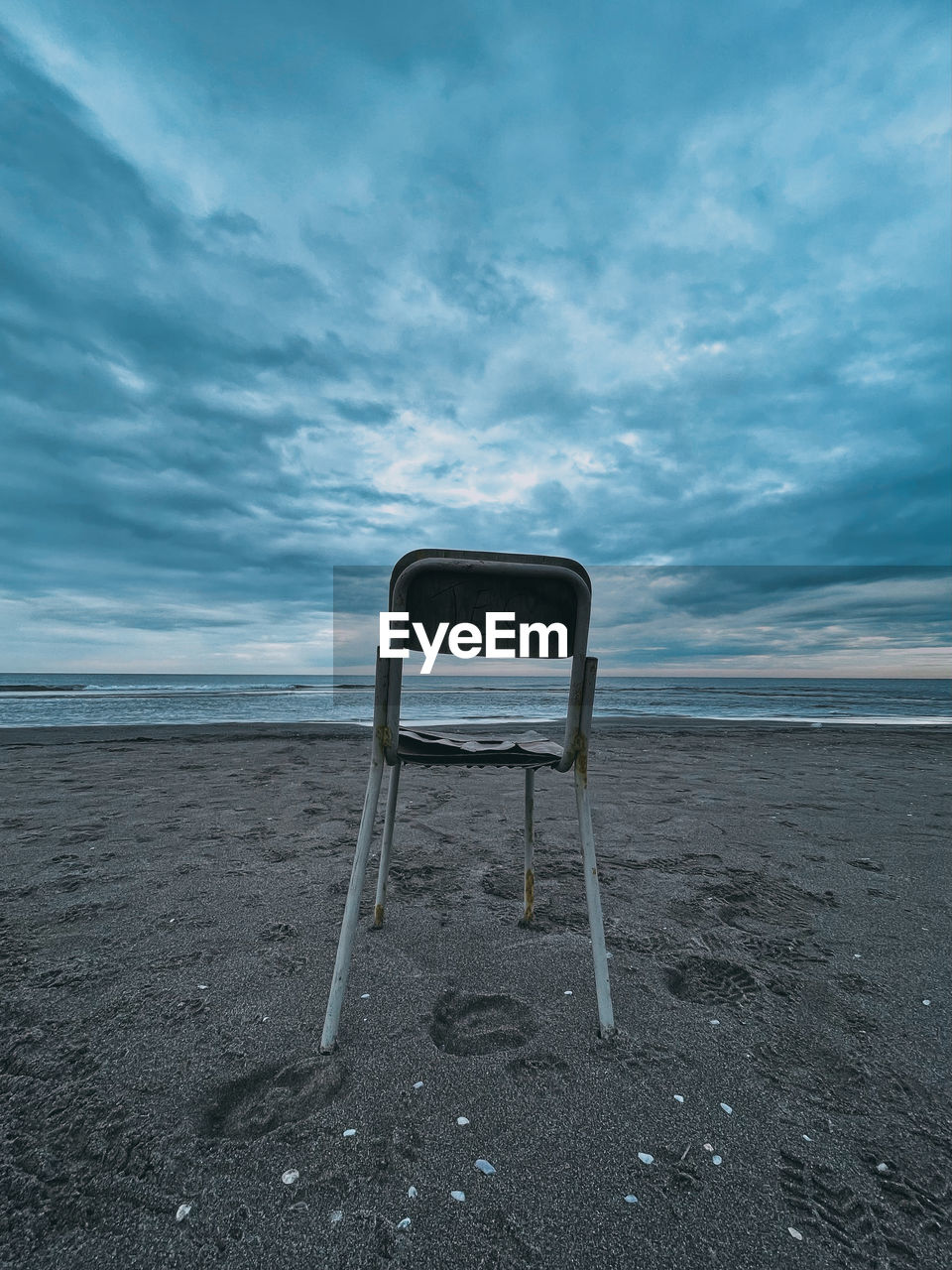 EMPTY CHAIR ON SHORE AGAINST SKY
