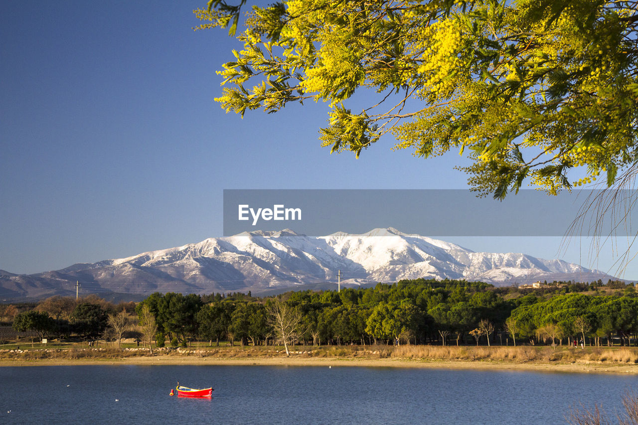 Scenic view of lake and mountains against clear blue sky