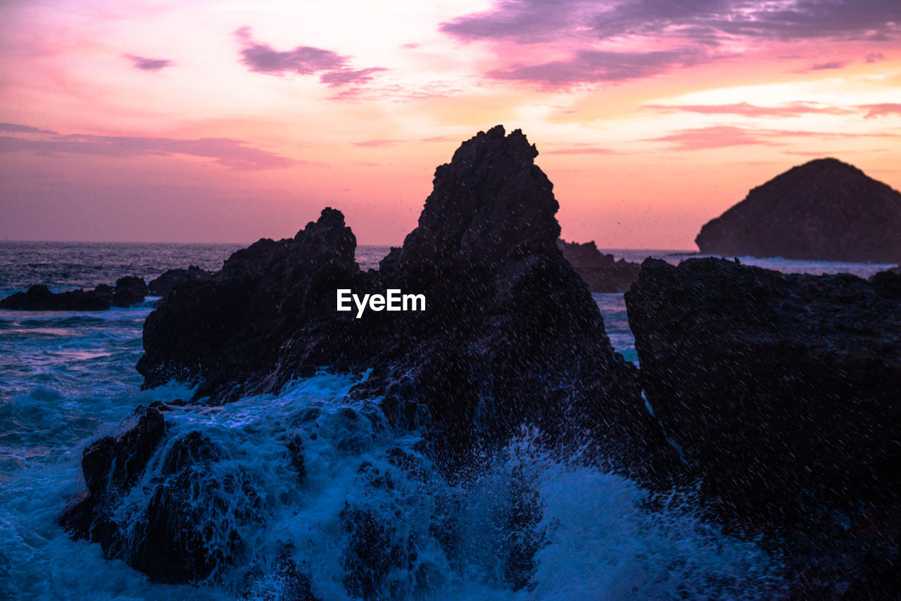 Rocks on sea shore against sky during sunset