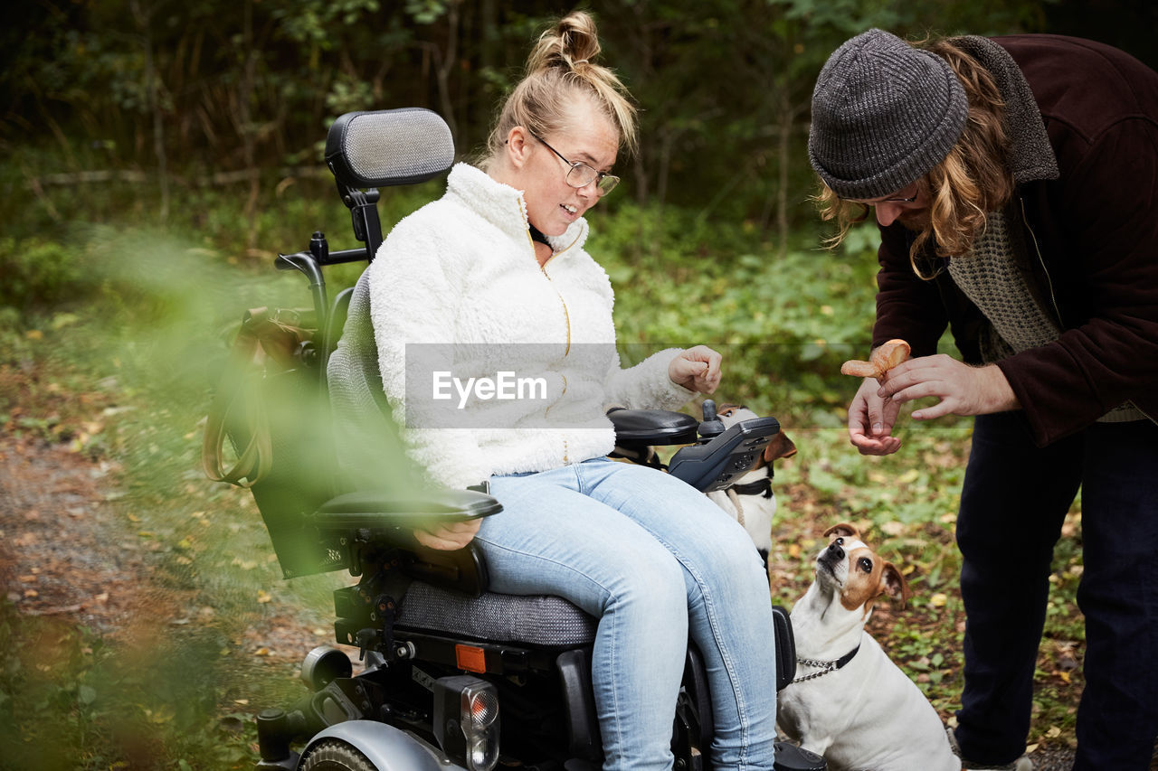 Disabled woman in wheelchair looking at caretaker holding mushroom in forest