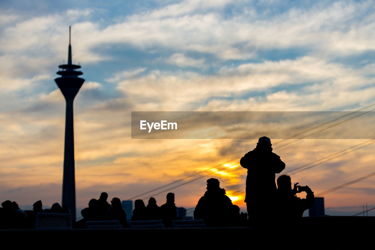 Silhouette people by rheinturm tower during sunset in city