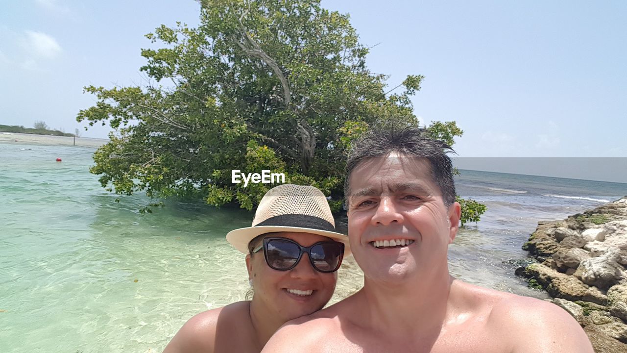 Portrait of smiling couple swimming in sea against sky