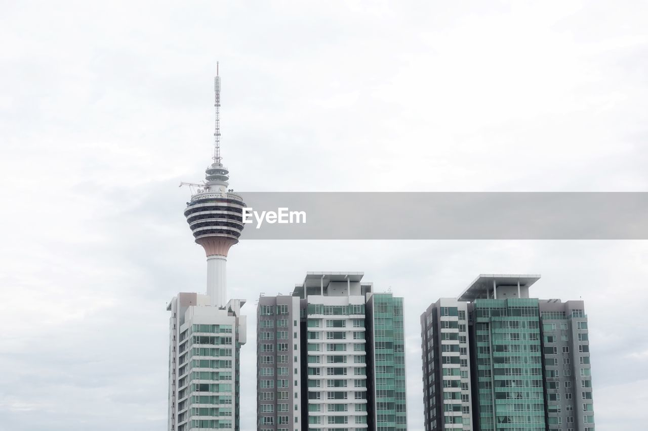 Kuala lumpur tv-tower surrounded by three block of flats. white, cloudy sky.