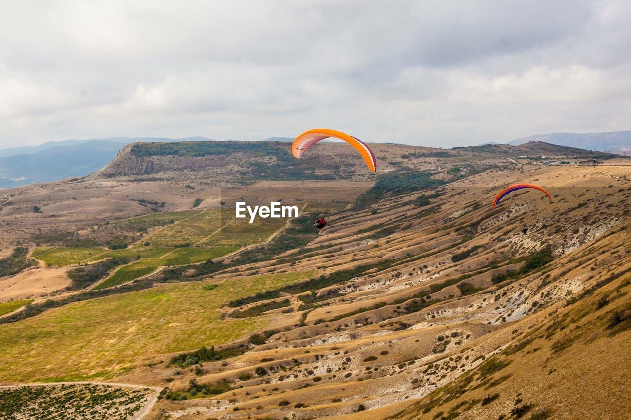 Person paragliding over mountains against cloudy sky