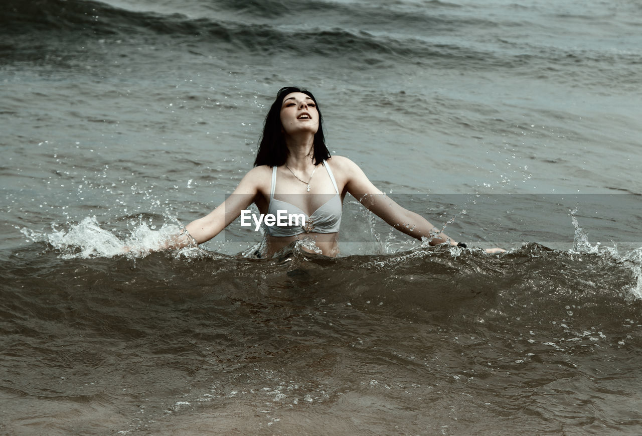 PORTRAIT OF YOUNG WOMAN IN WATER AT BEACH