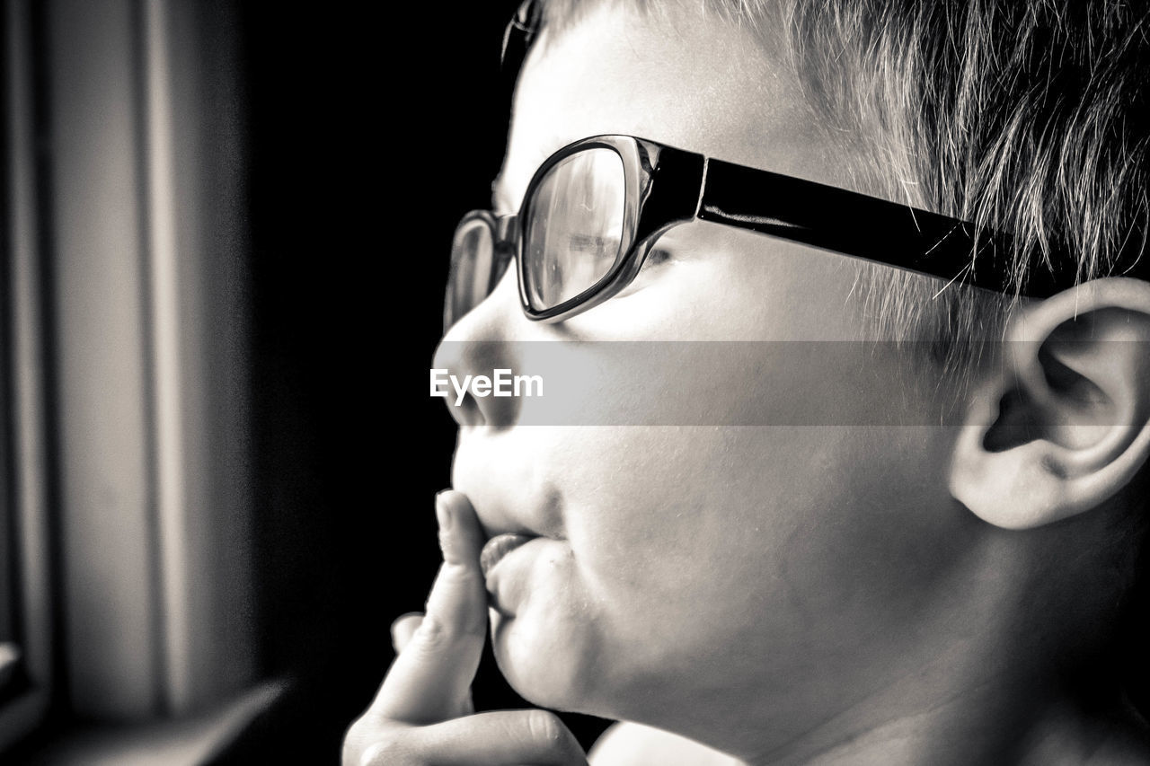 Close-up of boy wearing eyeglasses while looking through window at home