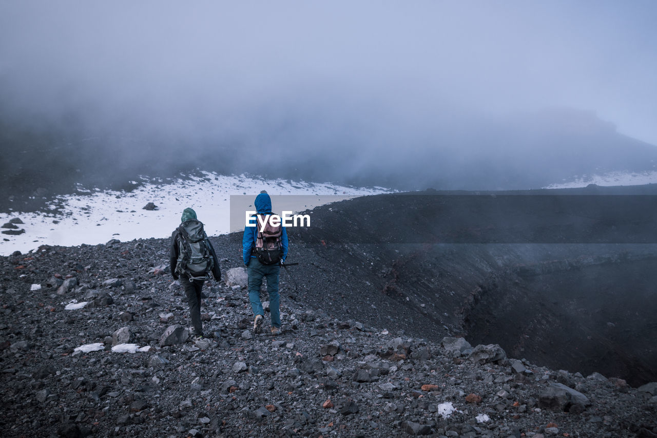 Rear view of male hikers hiking on mountain during winter