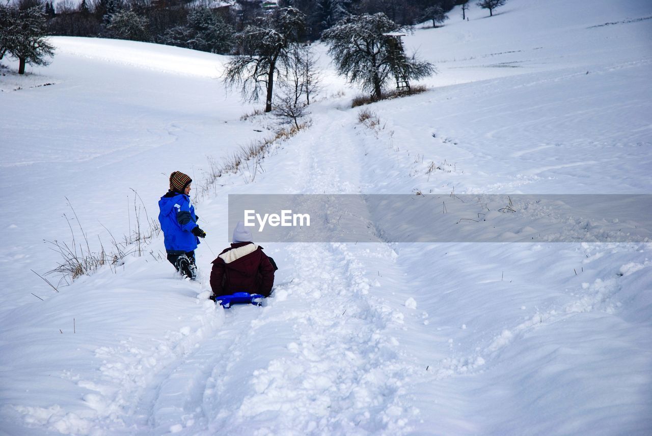 Boy pulling girl on sled on snow covered land
