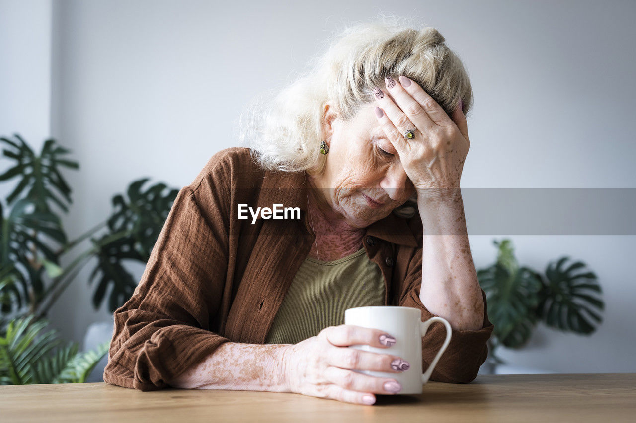 Upset senior woman with head in hand sitting at home