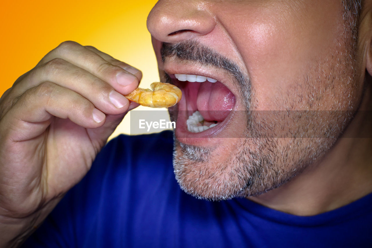 Close-up of a hungry man biting into a prawn. irresistible craving for food. yellow background.
