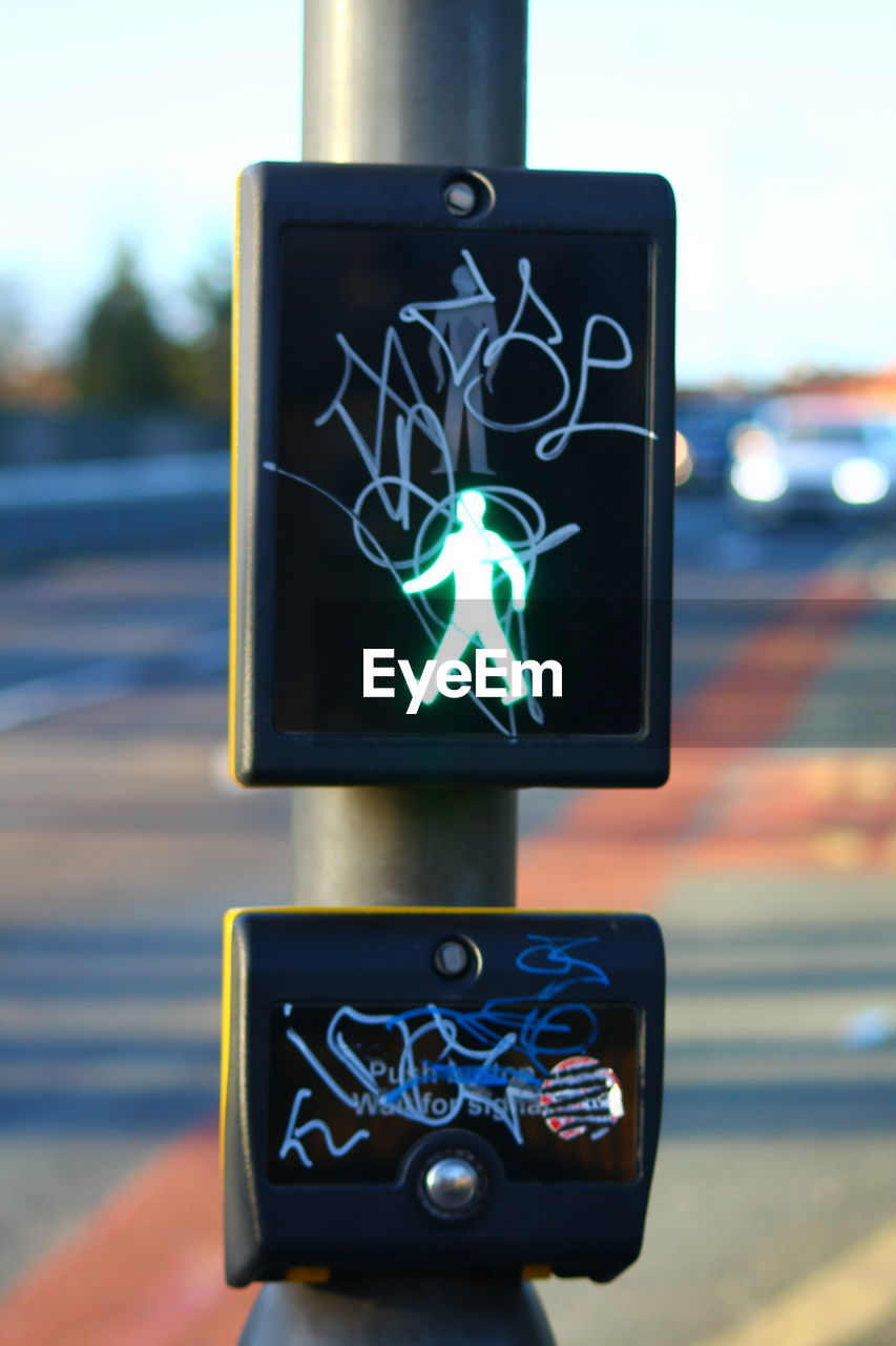 Graffiti on illuminated pedestrian crossing sign by road