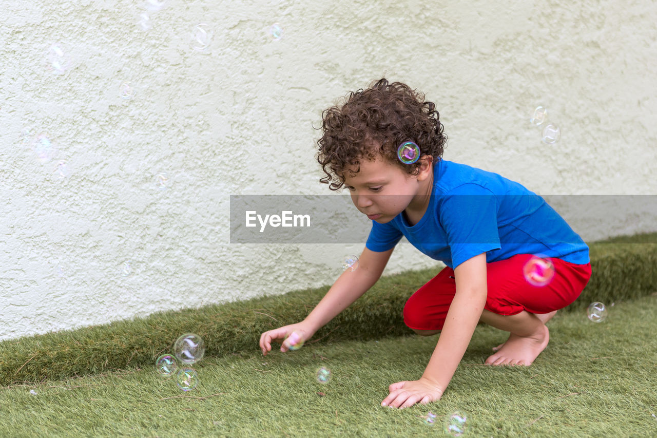 Beautiful 4-5 year old caucasian boy with curly hair in his backyard playing with soap bubbles