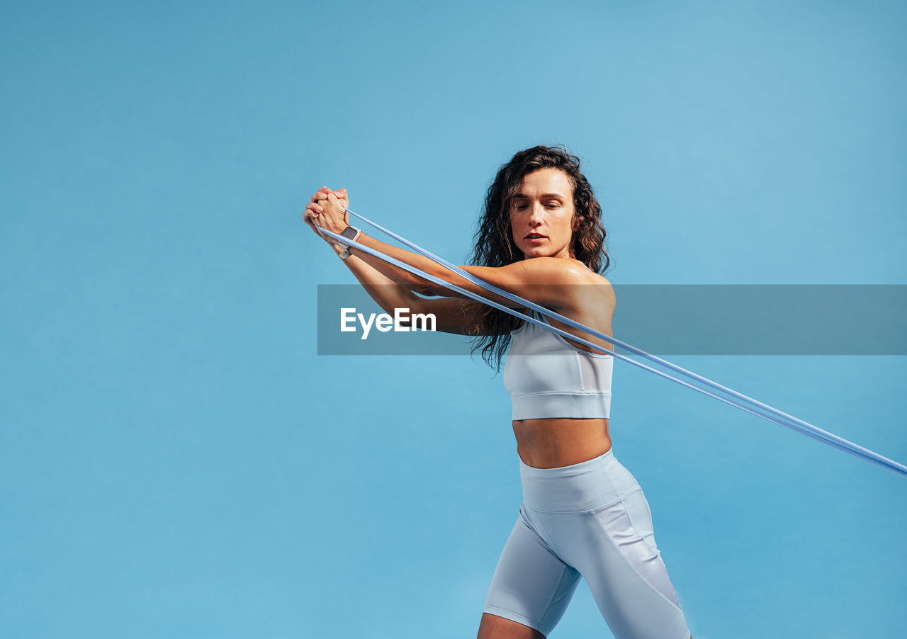 low angle view of young woman exercising against clear blue background