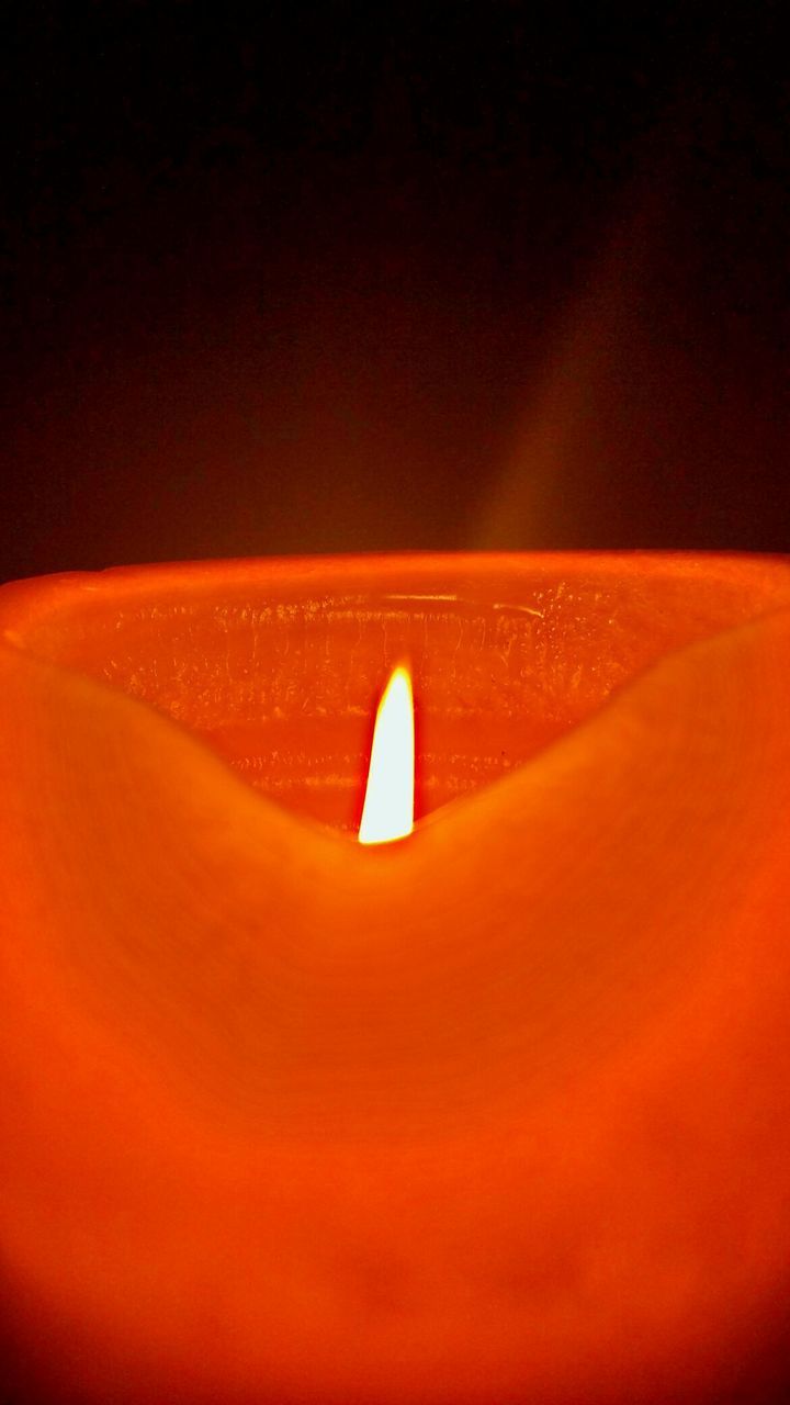 Close-up of burning orange candle against black background