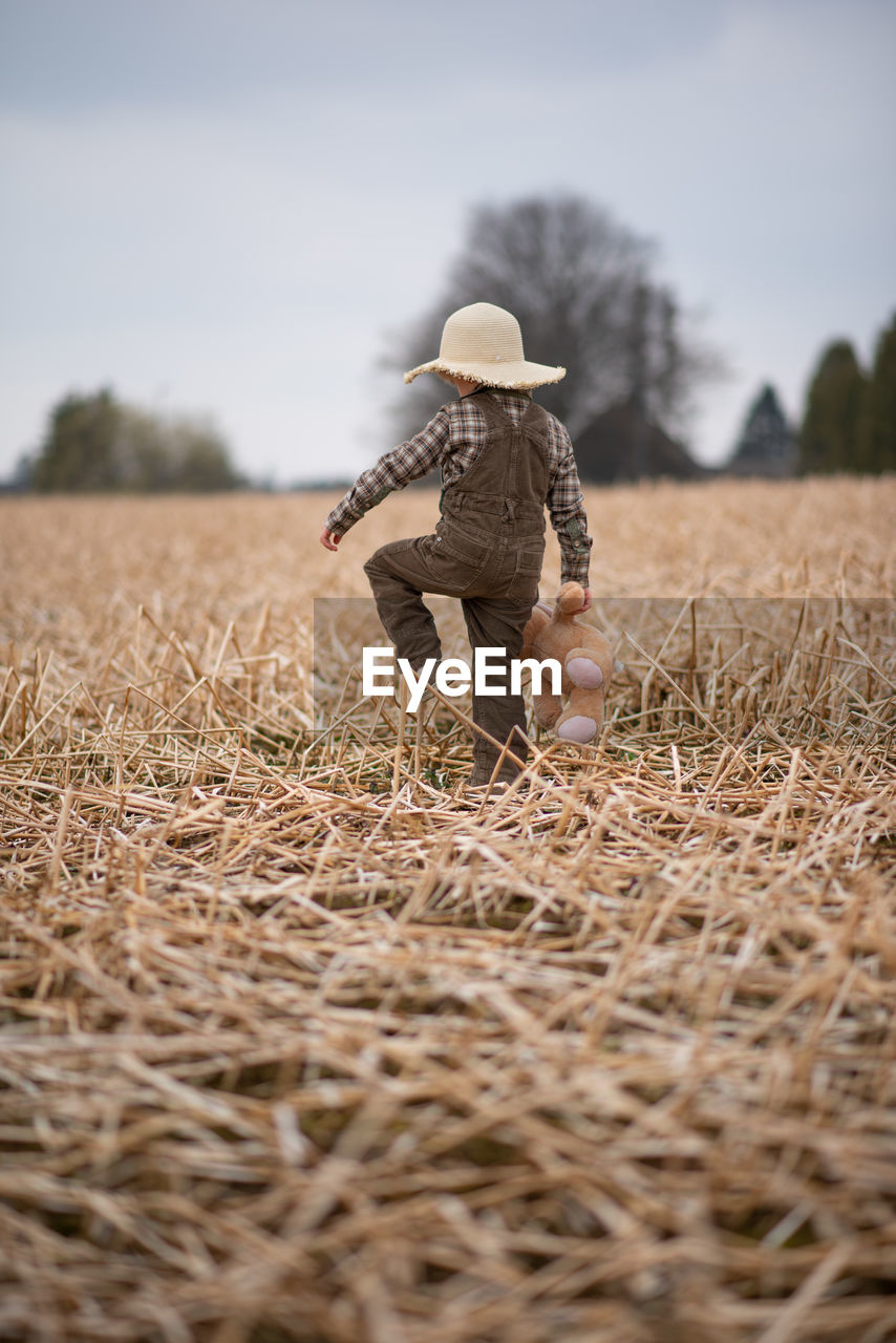 Back view of a boy walking in the field with a soft toy