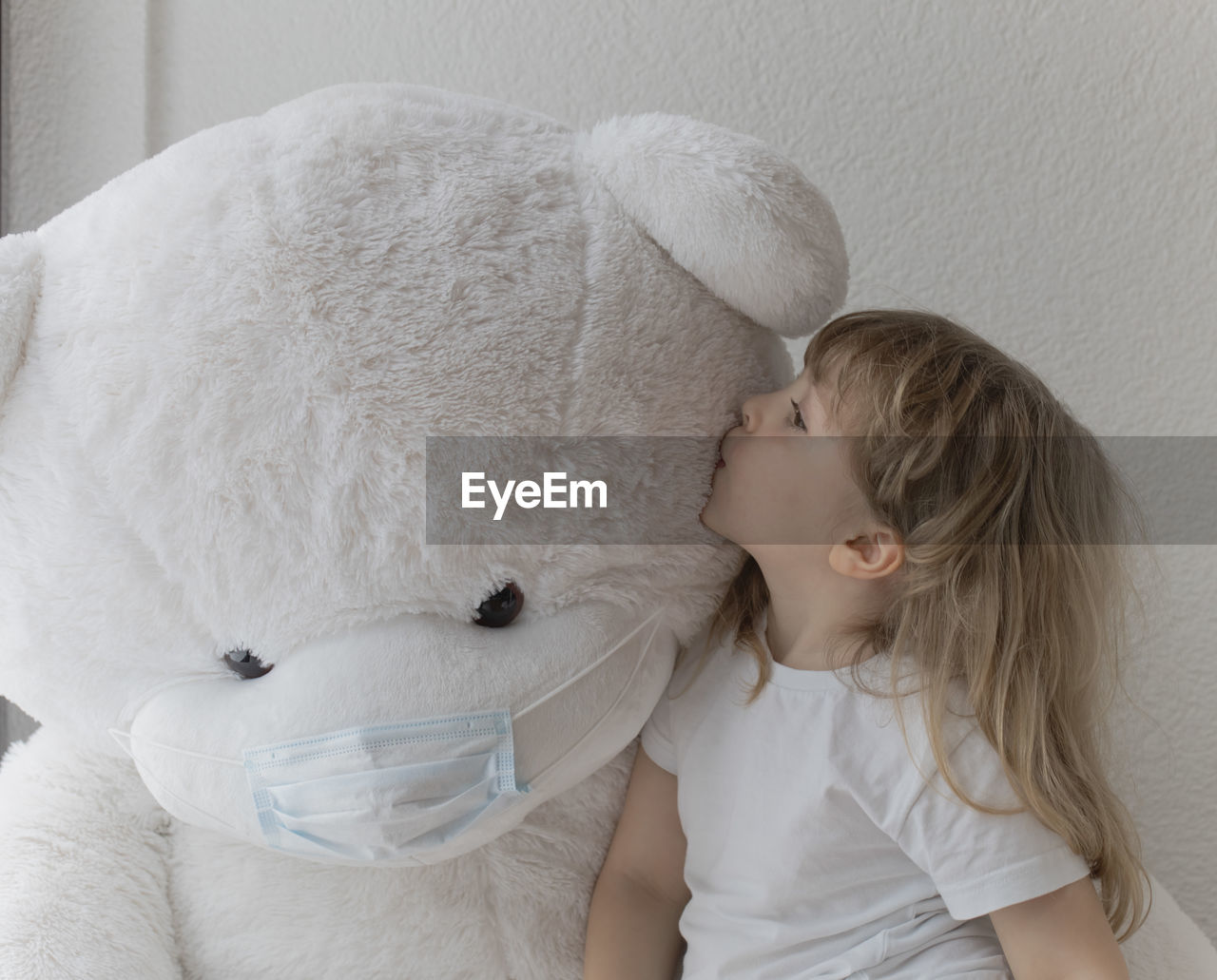 The girl of 5 is kissing her white plush teddy bear.